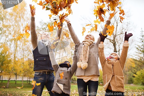 Image of happy family playing with autumn leaves in park
