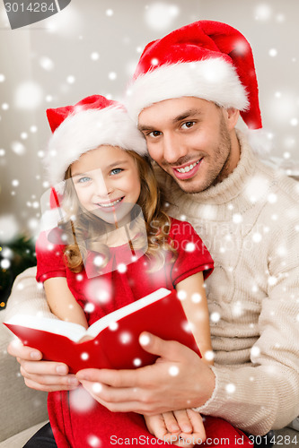 Image of smiling father and girl in santa hats reading book