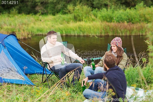 Image of group of smiling tourists drinking beer in camping