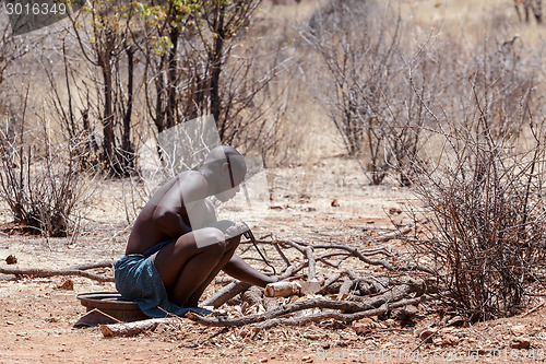 Image of Himba man adjusts wooden souvenirs in fireplace for tourists