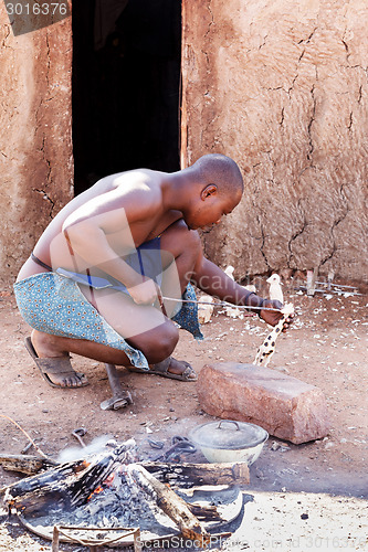 Image of Himba man adjusts wooden souvenirs in fireplace for tourists