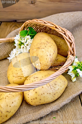 Image of Potatoes yellow in basket with flower on sackcloth and board