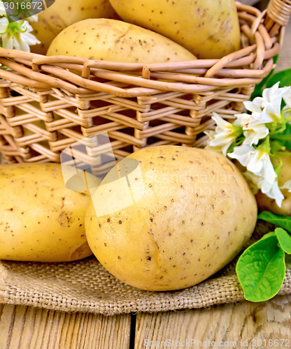 Image of Potatoes yellow with flower and basket on wooden board