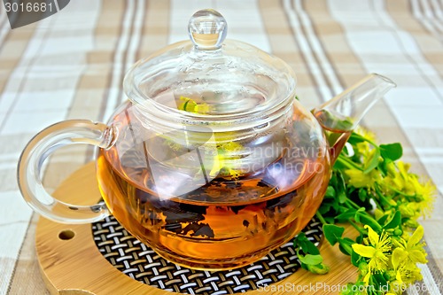 Image of Herbal tea from tutsan in glass teapot on linen tablecloth