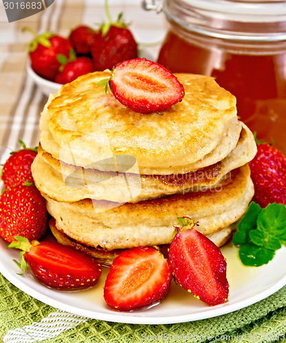 Image of Flapjacks with strawberries and honey on tablecloth