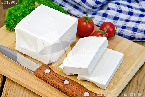 Image of Feta with tomato and knife on wooden board