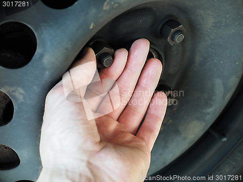 Image of Person checking rusty nuts on a steel rim of a vehicle