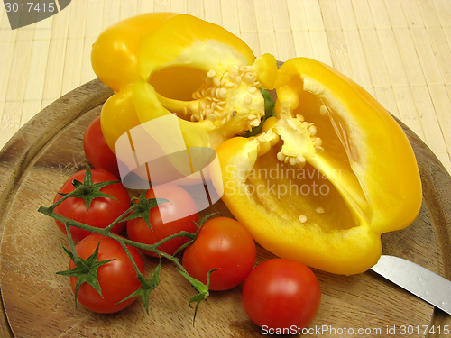 Image of Halved yellow pepper and tomatoes on wooden plate  with knife