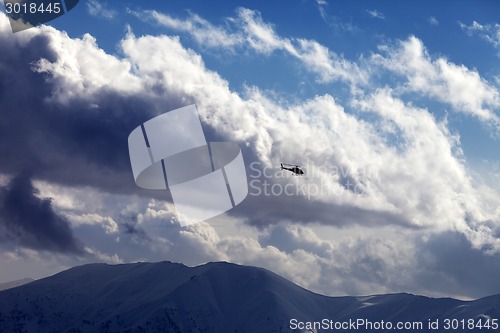 Image of Helicopter in cloudy sky and winter mountains