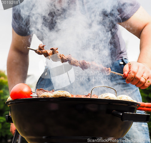Image of Chef covered in smoke grilling skewers of meat and vegetables ov