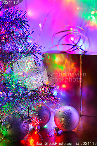 Image of Christmas tree, balls, box, lit by fairy lights