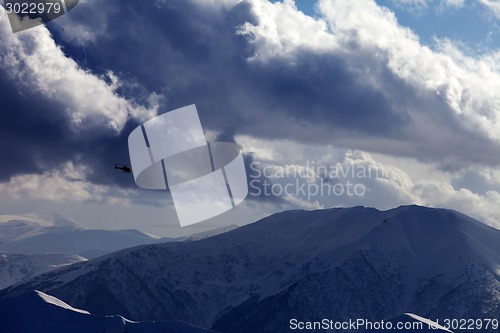 Image of Helicopter in winter mountains and cloudy sky in evening