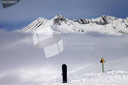 Image of Warning sing, snowboard on off-piste and mountains in fog