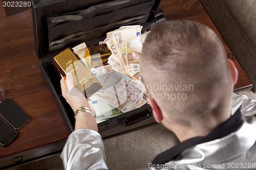 Image of man with suitcase full of money and gold