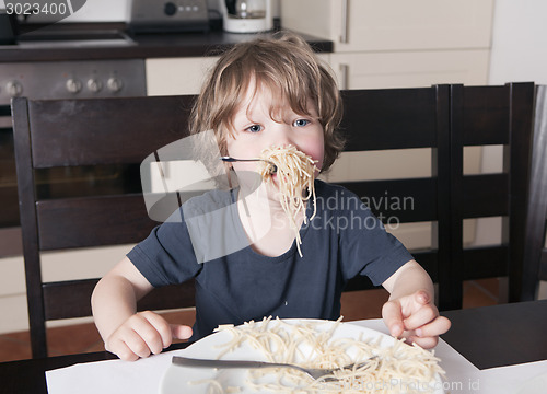 Image of Boy has mouth full of pasta in kitchen