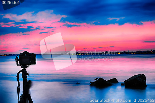 Image of Dslr camera shooting on a beutiful seascape with blue red sky su