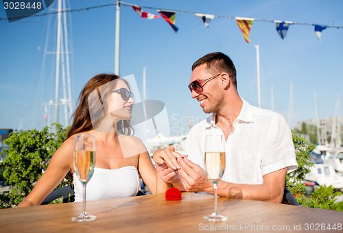 Image of smiling couple with champagne and gift at cafe