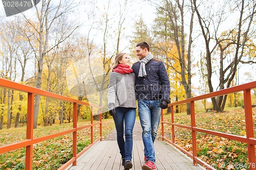 Image of smiling couple hugging on bridge in autumn park