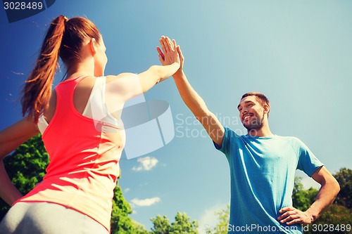 Image of two smiling people making high five outdoors