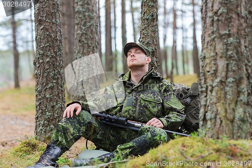 Image of soldier or hunter with gun sleeping in forest