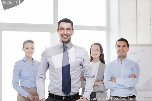 Image of smiling businessman in office with team on back