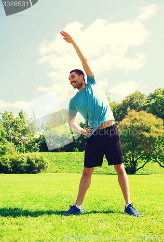 Image of smiling man stretching outdoors