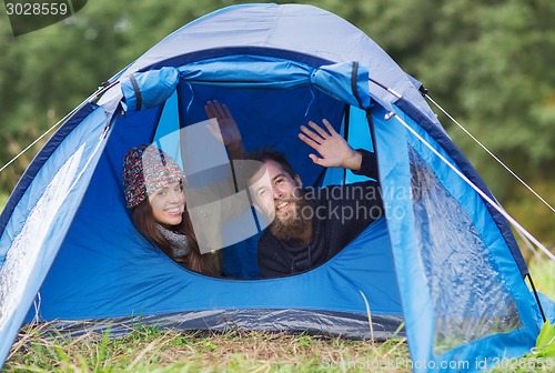 Image of smiling couple of tourists looking out from tent