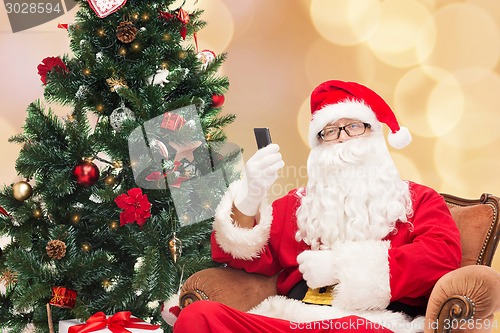 Image of santa claus with smartphone and christmas tree
