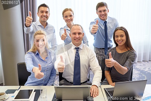 Image of business people showing thumbs up in office