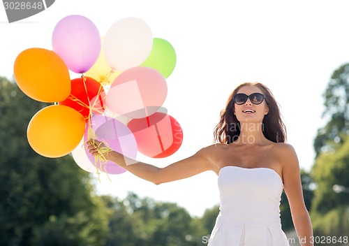 Image of smiling young woman in sunglasses with balloons