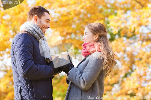 Image of smiling couple with coffee cups in autumn park