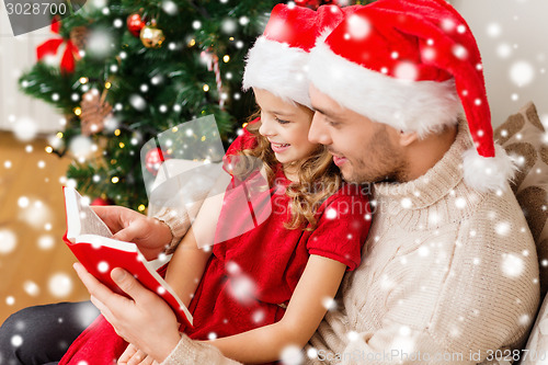 Image of smiling father and girl in santa hats reading book