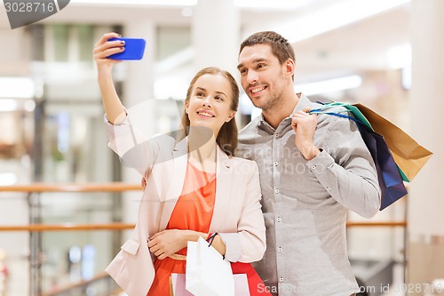 Image of happy couple with smartphone taking selfie in mall