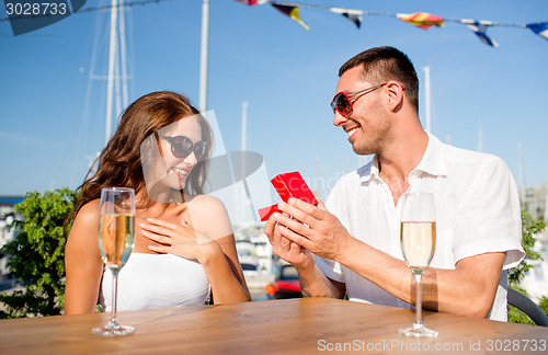 Image of smiling couple with champagne and gift at cafe