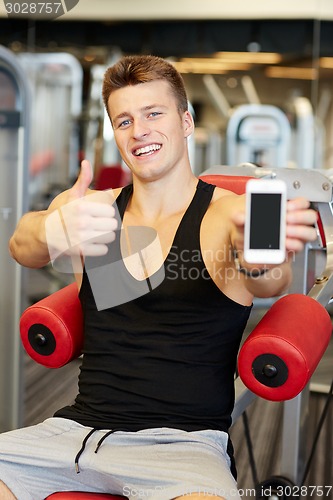 Image of smiling young man with smartphone in gym