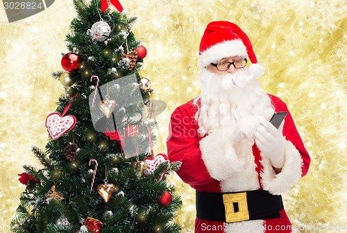 Image of santa claus with smartphone and christmas tree