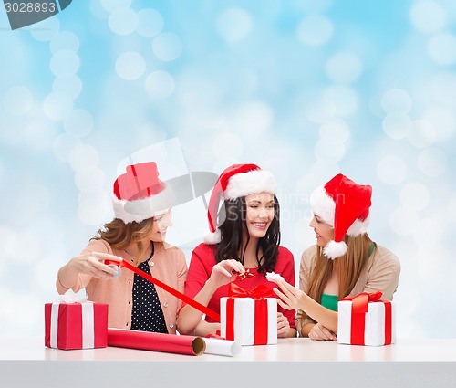 Image of smiling women in santa helper hats packing gifts