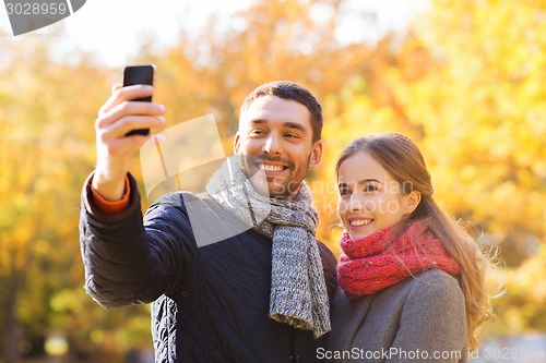 Image of smiling couple with smartphone in autumn park