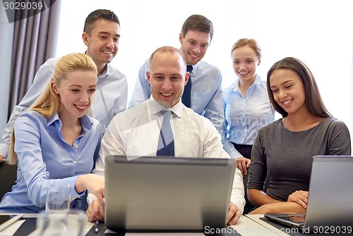 Image of smiling business people with laptop in office