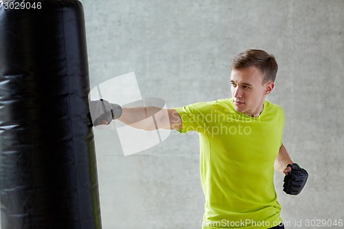 Image of young man in gloves boxing with punching bag