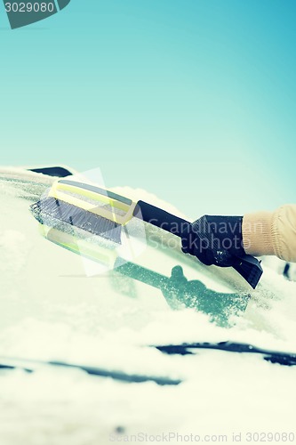 Image of man cleaning snow from car windshield with brush