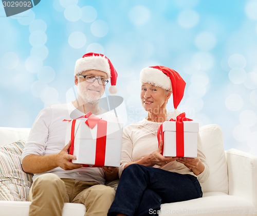 Image of happy senior couple in santa hats with gift boxes
