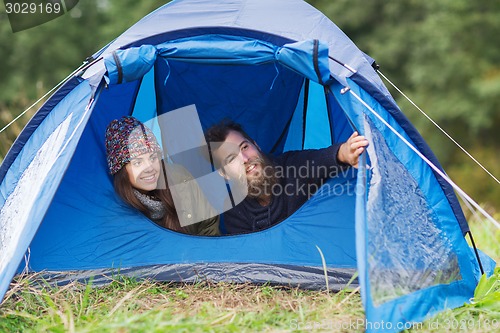 Image of smiling couple of tourists looking out from tent