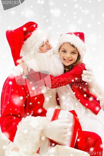 Image of smiling girl hugging santa claus with gift at home