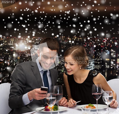 Image of smiling couple with smartphone at restaurant