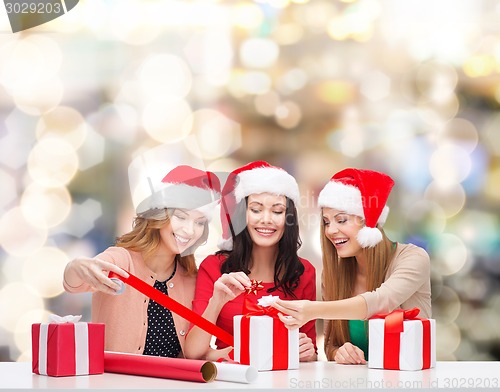 Image of smiling women in santa helper hats packing gifts