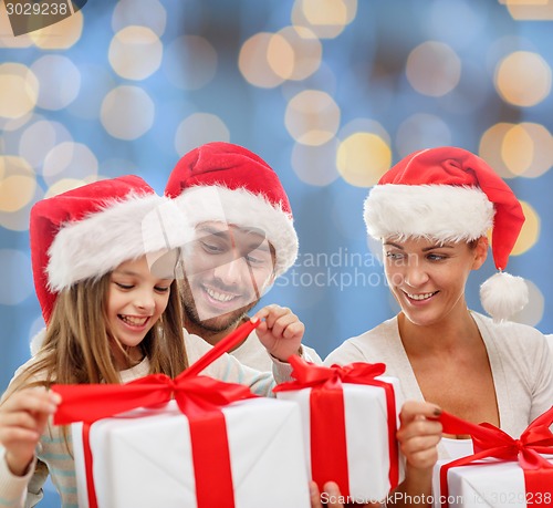 Image of happy family in santa hats sitting with gift boxes