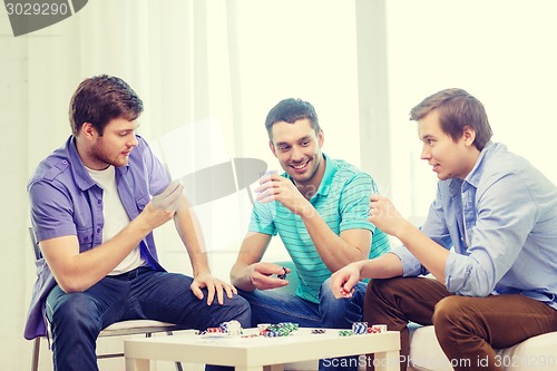 Image of happy three male friends playing poker at home