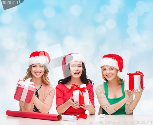 Image of smiling women in santa helper hats packing gifts