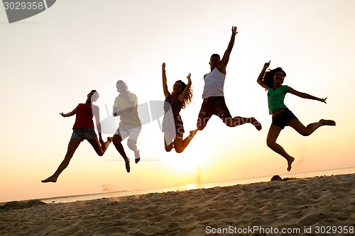 Image of smiling friends dancing and jumping on beach